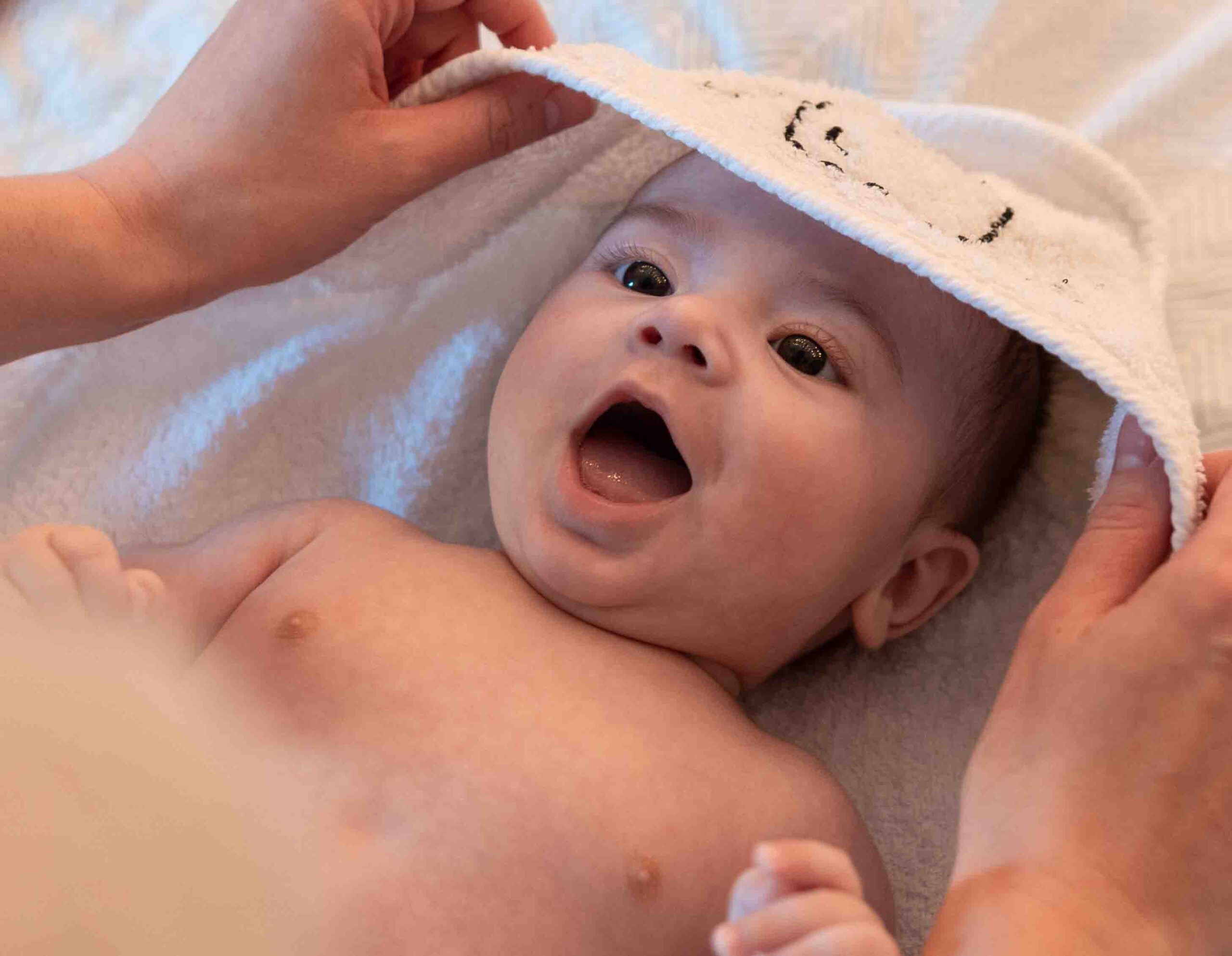 Neonato sdraiato con mamma che lo copre con un asciugamano, esempio di plagiocefalia trattabile con approccio osteopatico pediatrico