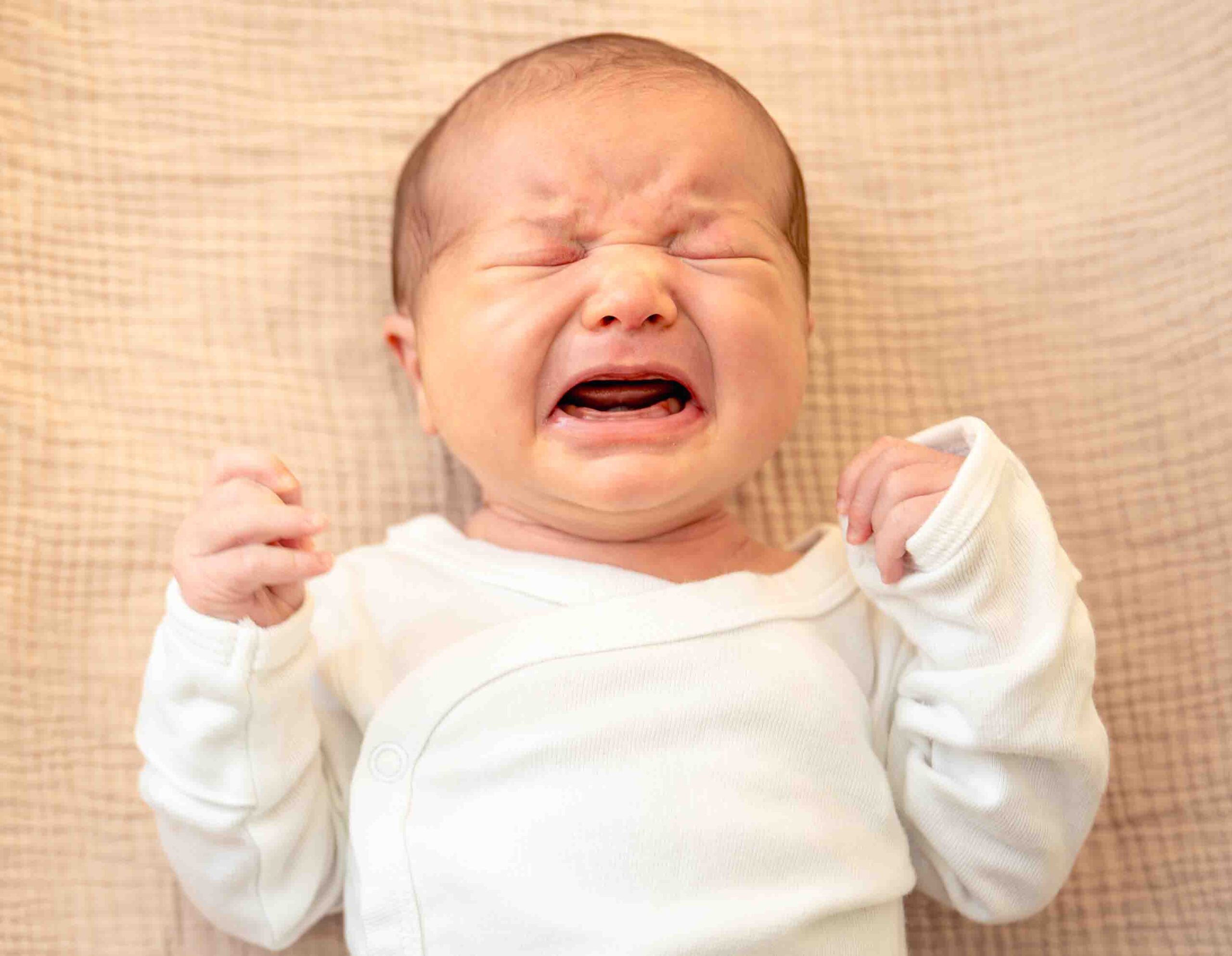 Neonato che piange disteso, simbolo di coliche e rigurgiti ricorrenti trattabili con approccio osteopatico pediatrico